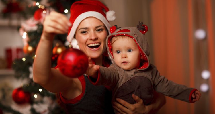 Happy mother showing Christmas ball  to baby near Christmas tree