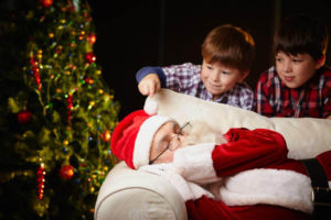 Cute siblings looking at Santa Claus sleeping by xmas tree, one of them touching him